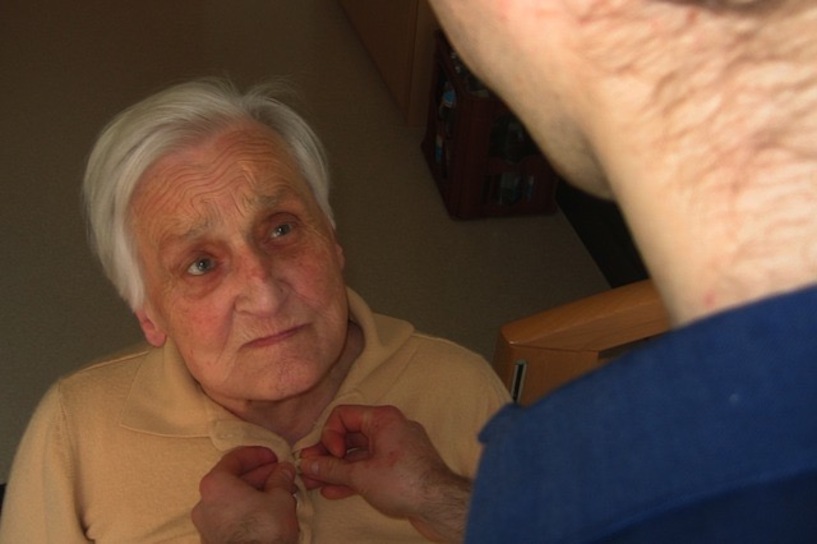 Ein Pfleger hilft beim Anziehen. Oma, anziehen, Pflege, Demenz, Bluse, Knopf